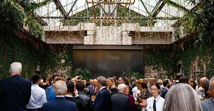 a large group of people standing around each other in a room with plants growing on the walls