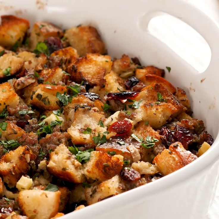 a white casserole dish filled with stuffing and cranberries, garnished with parsley