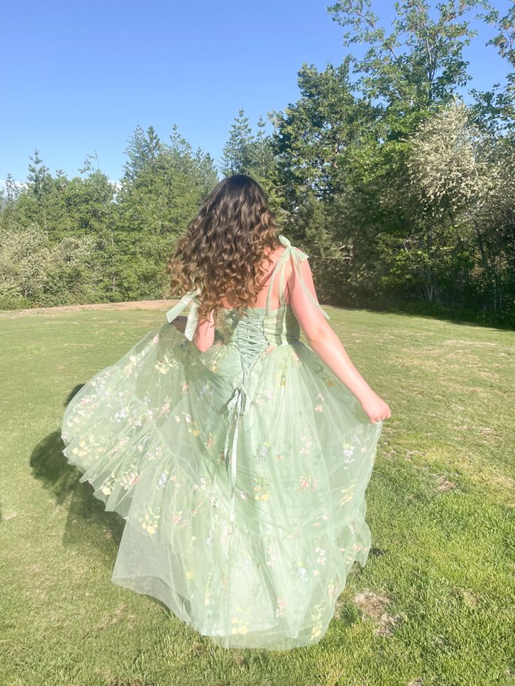 a woman in a green dress is walking through the grass with her back to the camera