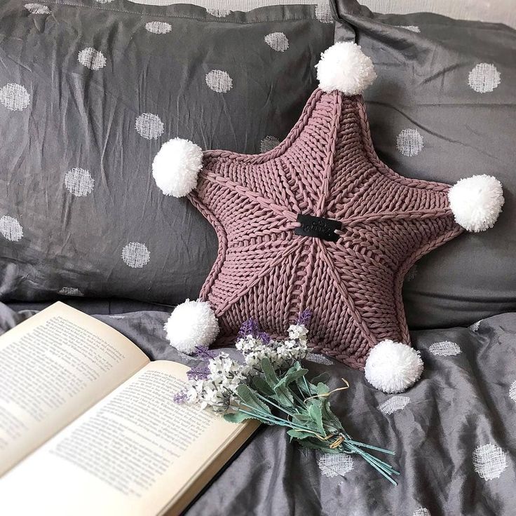 an open book on a bed with a star pillow and pom - poms