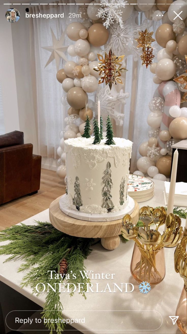 a white cake sitting on top of a table next to balloons and trees in the background