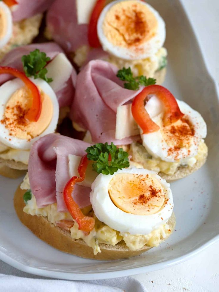 an open face sandwich topped with ham, eggs and peppers on a white platter