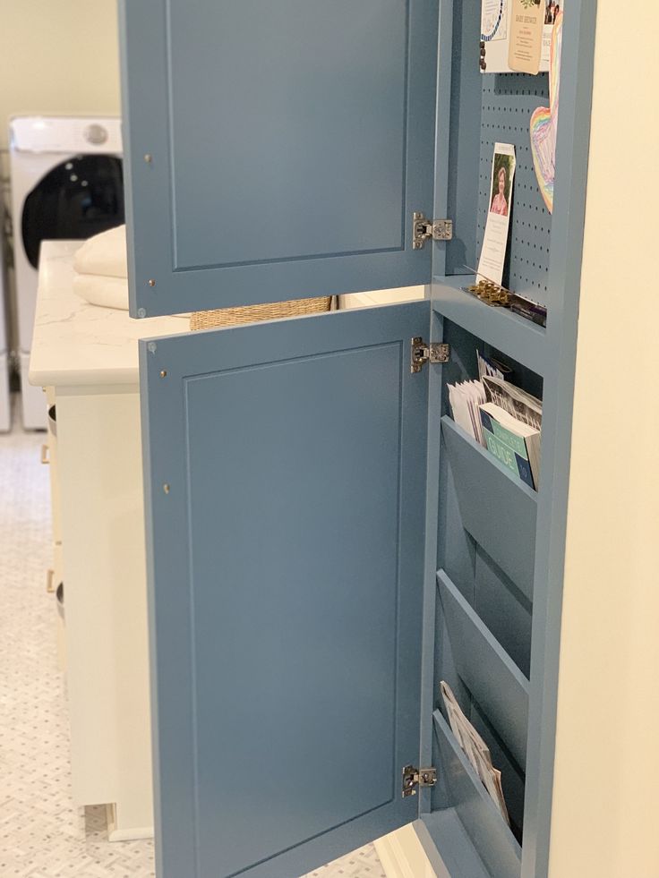 an open blue cabinet in the middle of a white floored room with papers on it