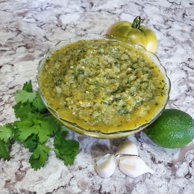 a glass bowl filled with green sauce next to two lemons and an avocado