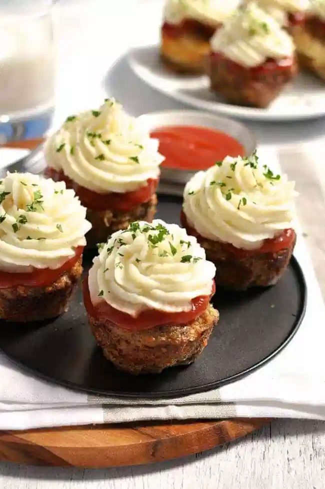 several small cupcakes with white frosting and toppings on a black plate