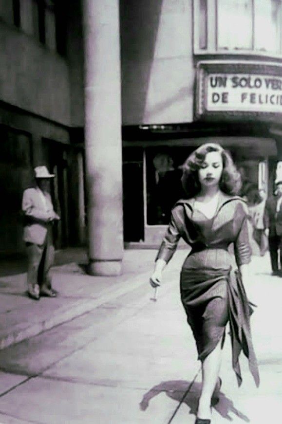 an old photo of a woman walking down the street in front of a movie theater