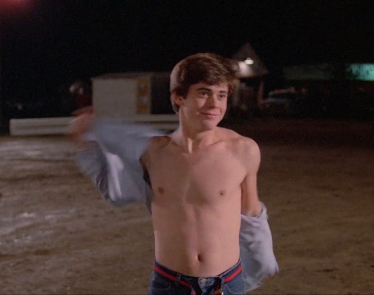 a shirtless young man holding his arms out in front of the camera at night