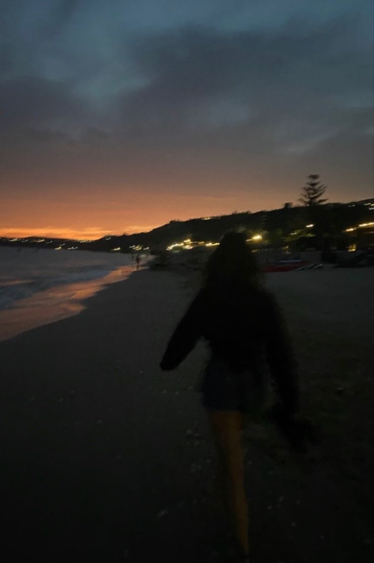 a woman walking on the beach at night with her back turned to the camera,