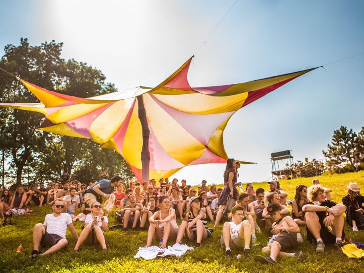 a group of people sitting on top of a lush green field under a large kite