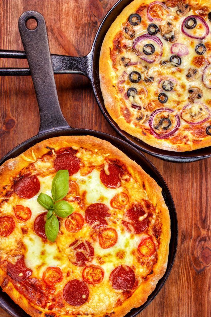 two pizzas sitting in pans on top of a wooden table