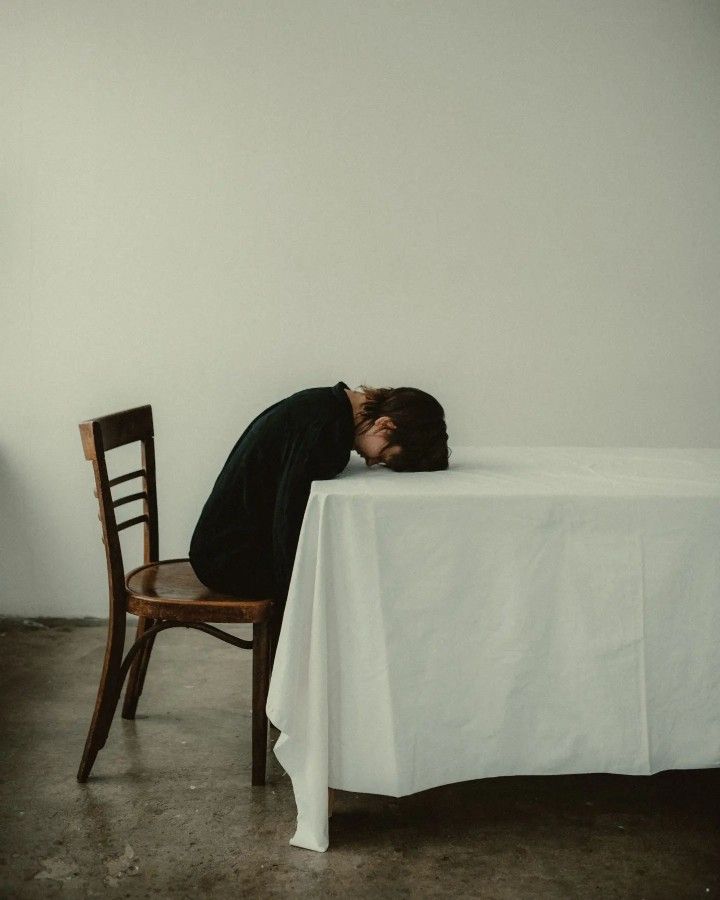 a person is sleeping on a table with a chair in front of them and a white sheet covering the table