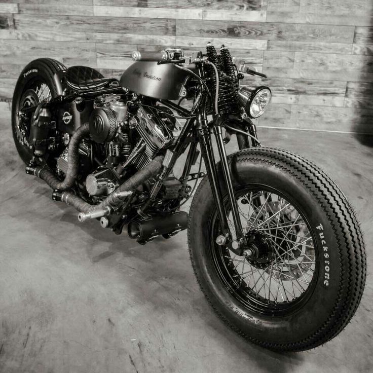 a black and white photo of a motorcycle parked in front of a brick wall with exposed pipes