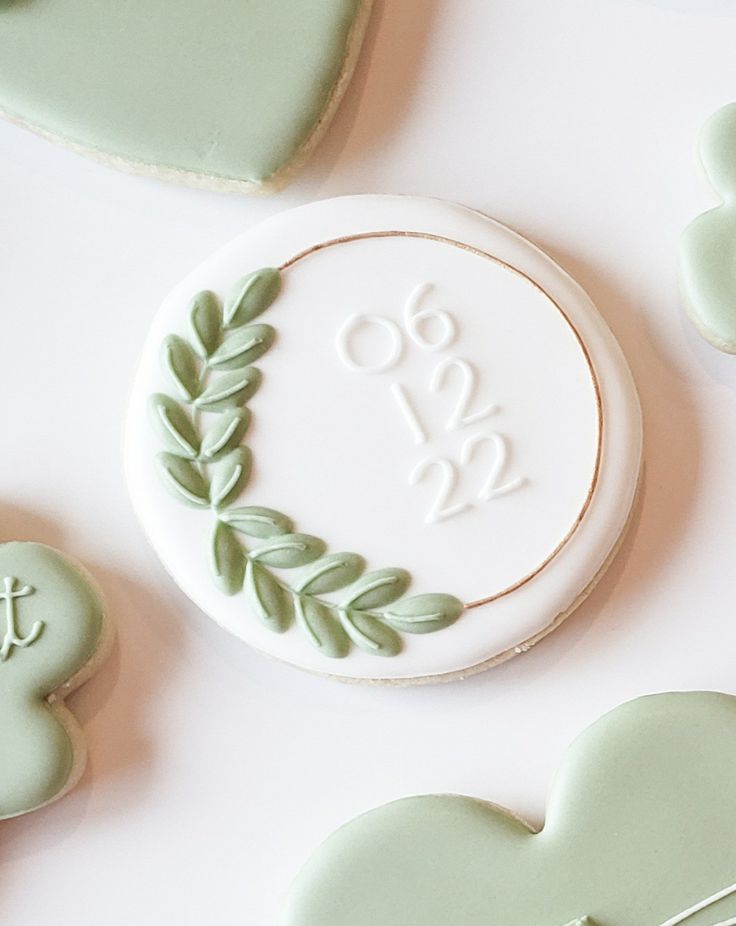 cookies decorated with green leaves and monograms are arranged on a white table top