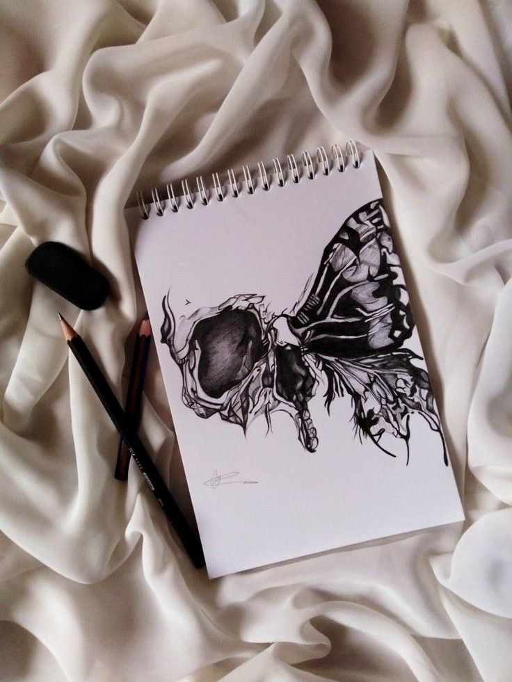 a spiral notebook with a drawing of a butterfly on it next to two pencils