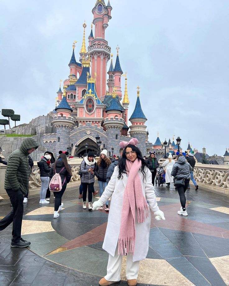 a woman standing in front of a castle with lots of people walking around it on a cloudy day