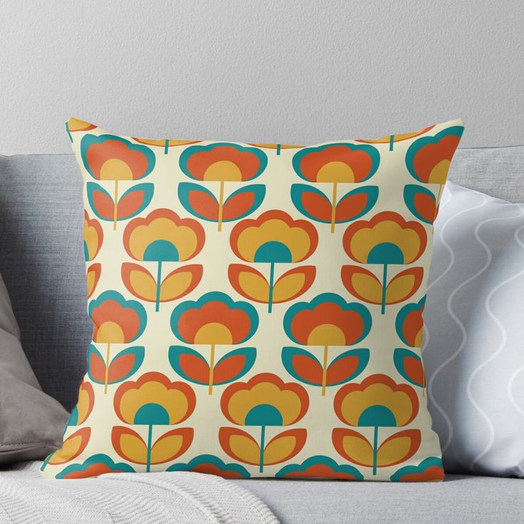 an orange, blue and yellow flower pattern on a white background throw pillow sitting on a couch