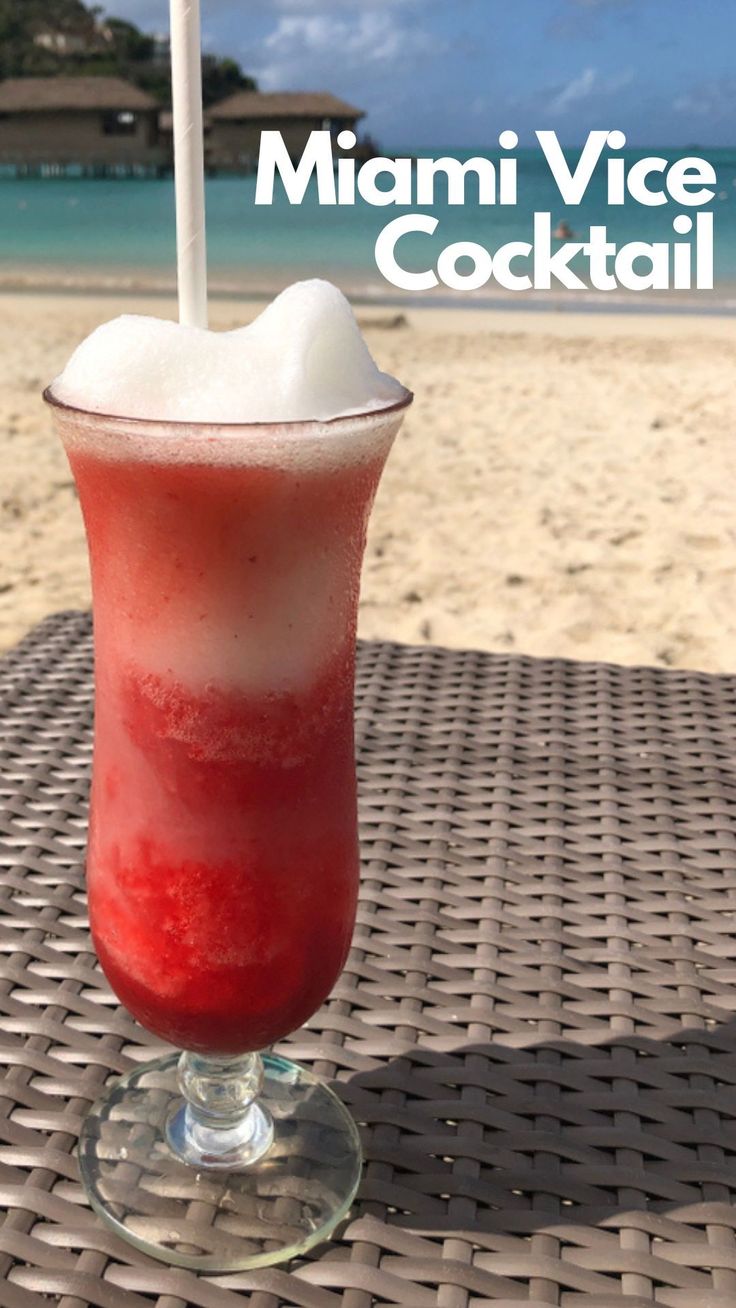 a red drink sitting on top of a table next to the ocean with a straw in it