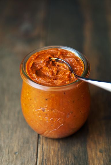 a jar filled with sauce sitting on top of a wooden table next to a spoon