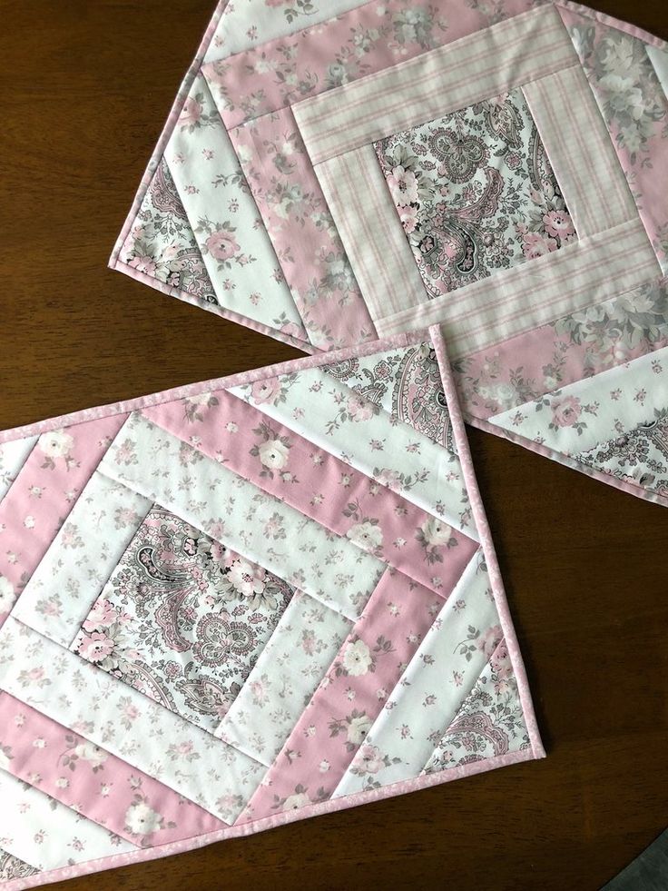 two pink and white quilted placemats sitting on top of a wooden table