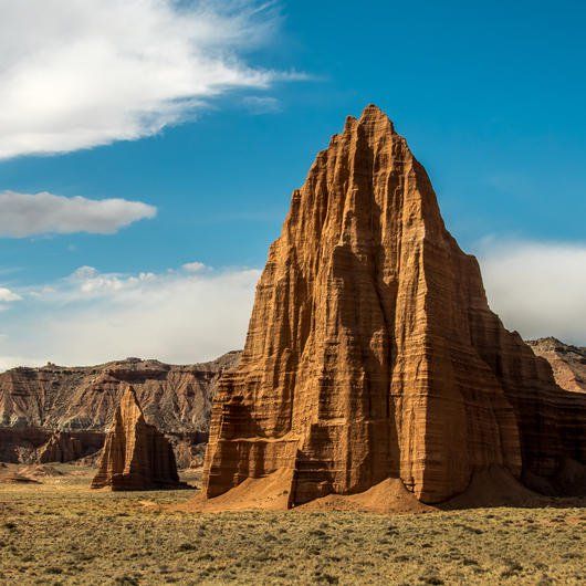 large rock formation in the middle of an arid area with blue sky and white clouds