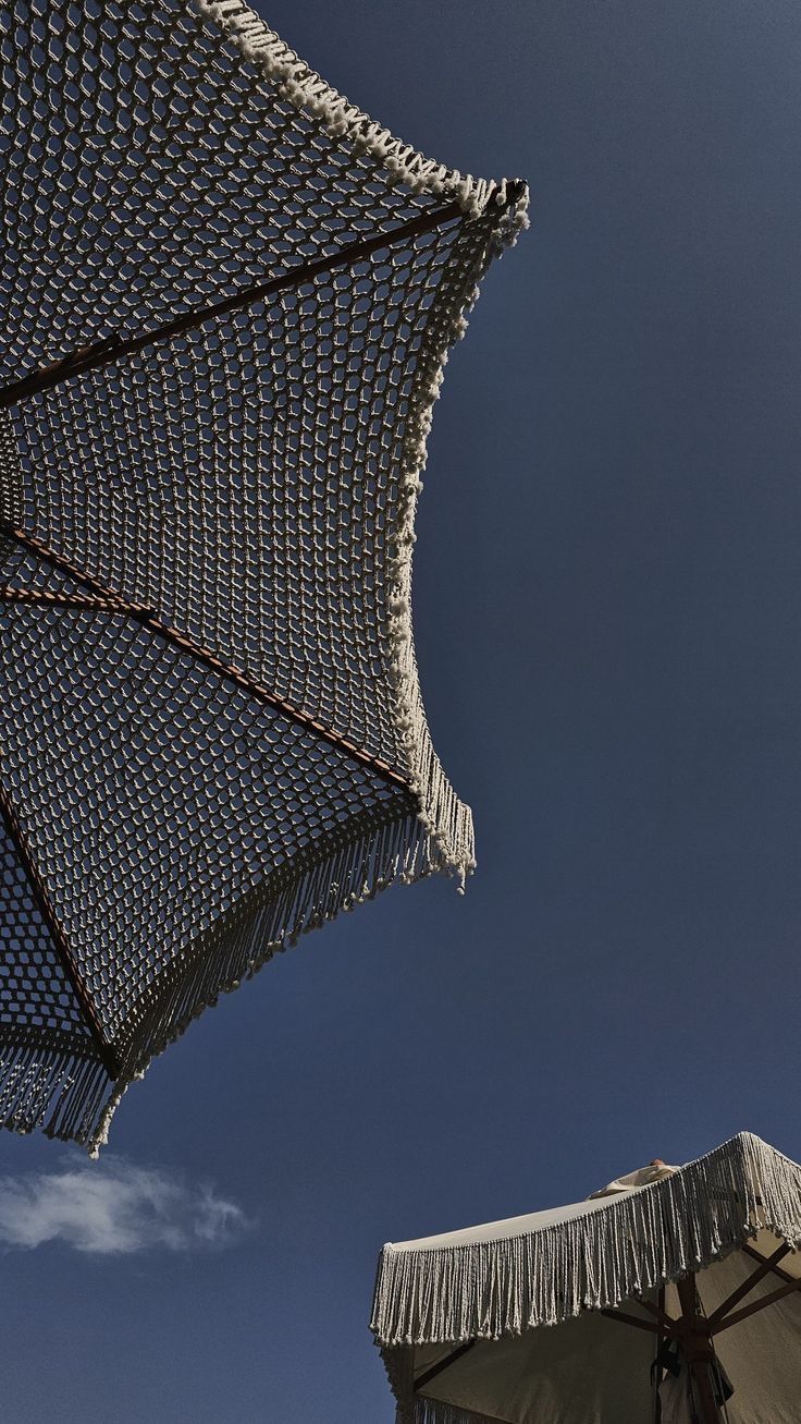 two umbrellas with fringe on them against a blue sky