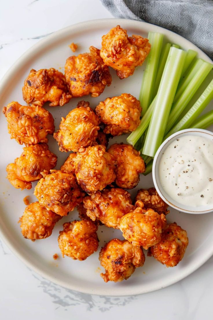 a white plate topped with tater tots next to celery and dip