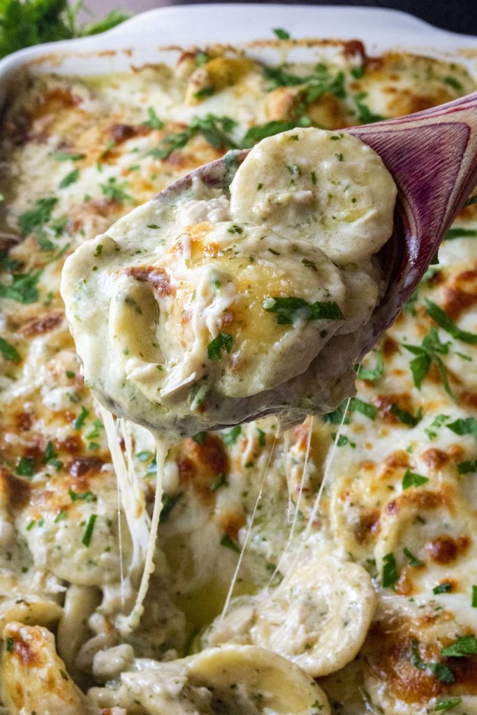 a wooden spoon scooping some food out of a casserole dish with broccoli and cheese