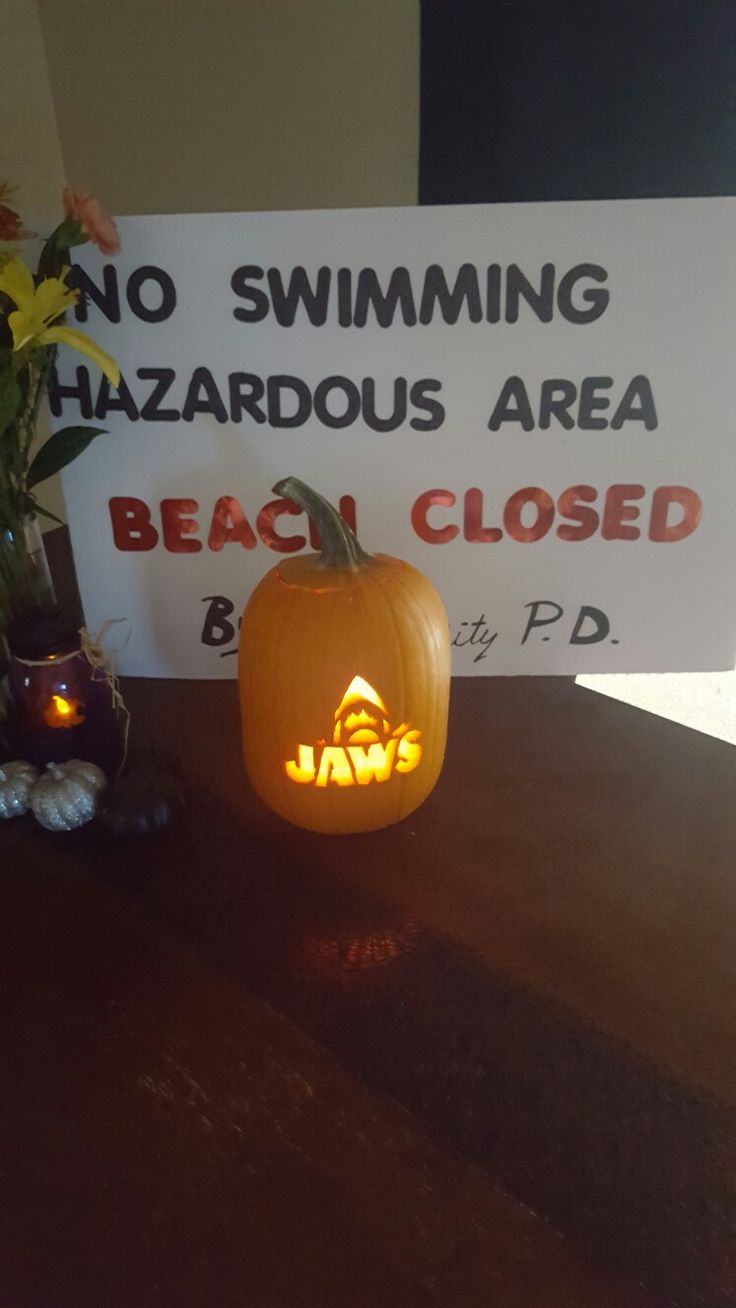 a carved pumpkin sitting next to a sign that says no swimming hazardous area beach closed