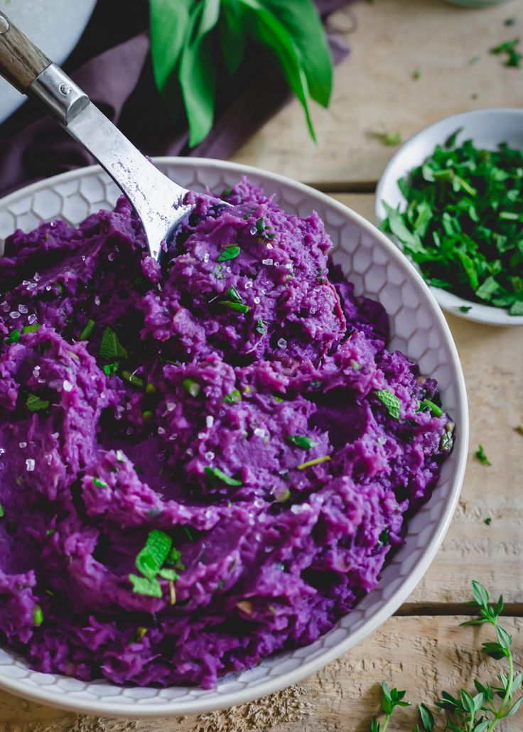 a white bowl filled with purple mashed potatoes and garnished with parsley