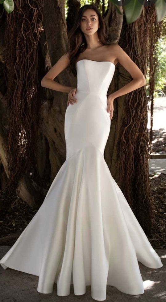 a woman standing in front of a tree wearing a white dress