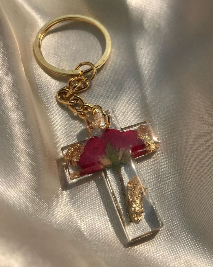 a cross keychain with a rose on it sitting on a white satin surface