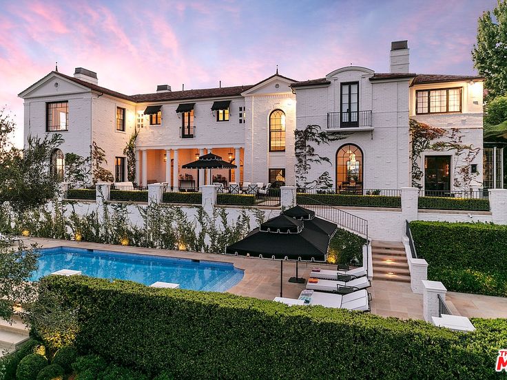 a large white house with a swimming pool in the front yard and landscaping around it