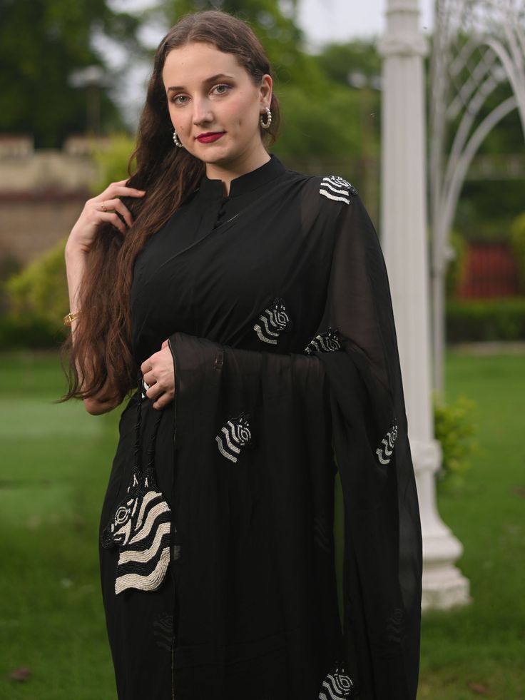 This is a three-piece black zebra saree set from the Ensembles collection. The black zebra saree is paired with a black sleeveless blouse. The blouse has front potli button opening, and a mandarin collar. There are beautiful zebra motifs of black and white bead work all over the saree. This saree set is crafted in pure organza fabric with contrast piping border. The outfit is completed with a heavily embellished, beadwork black and white zebra shape handbag. Elegant Black Pre-draped Saree With Mirror Work, Designer Sheer Dupatta Blouse In Black, Designer Black Blouse With Sheer Dupatta, Designer Black Blouse With Dupatta, Designer Black Pre-draped Saree For Eid, Designer Wear Black Pre-draped Saree For Eid, Black Pre-draped Saree With Mirror Work For Designer Wear, Black Anarkali Pre-draped Saree With Dupatta, Black Anarkali Pre-draped Saree For Eid