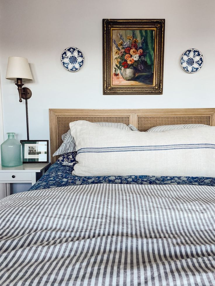 a bed with blue and white striped sheets in front of a painting on the wall