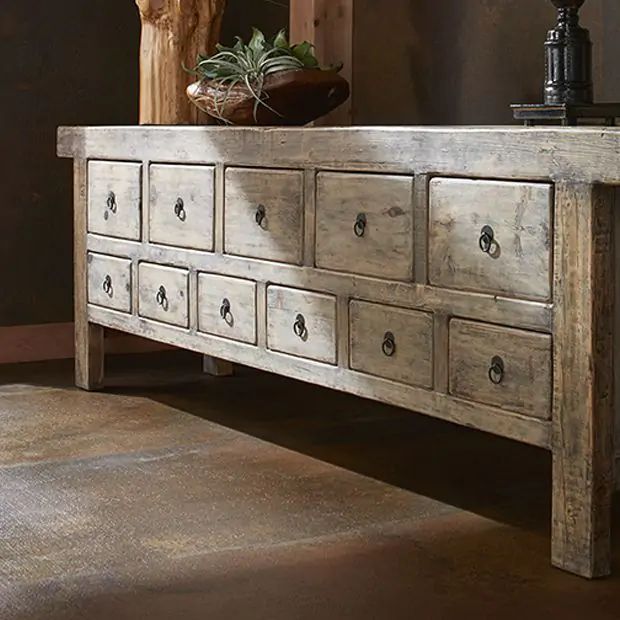 an old wooden dresser with many drawers and plants on it's top, in front of a brown wall