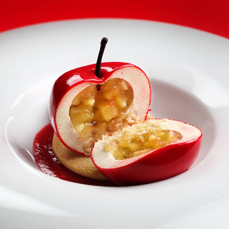 an apple is cut in half on a white plate with red sauce and fruit toppings