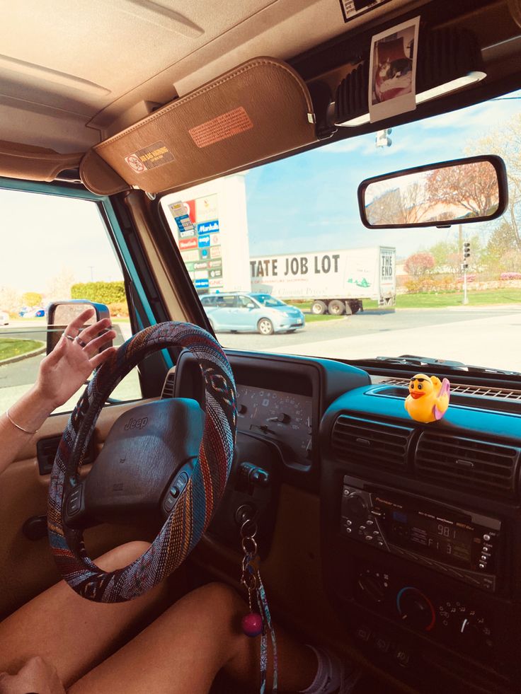 a person sitting in the drivers seat of a car holding a cell phone and steering wheel