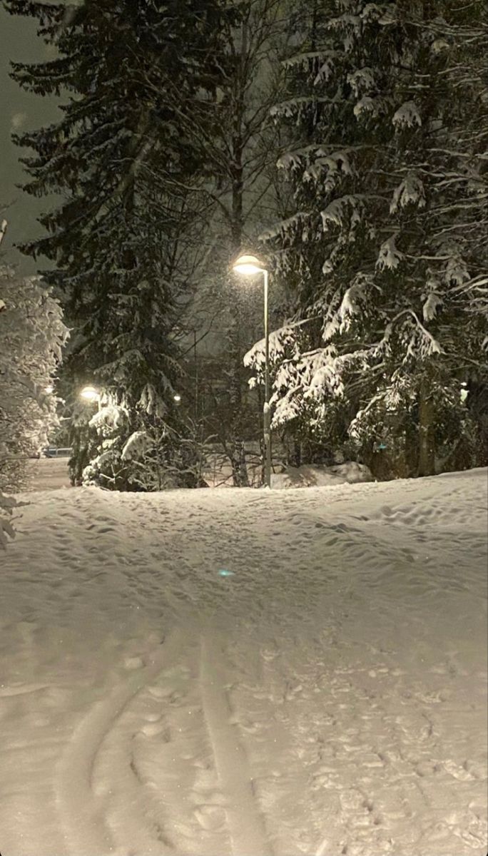 a man riding skis down a snow covered slope next to a street light at night