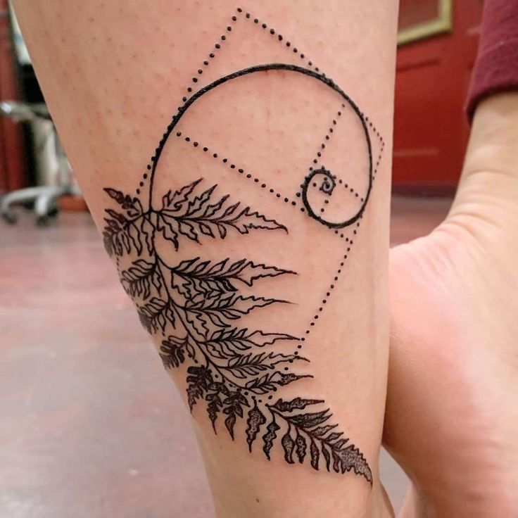 a woman's leg with a tattoo on it that has leaves and a spiral design