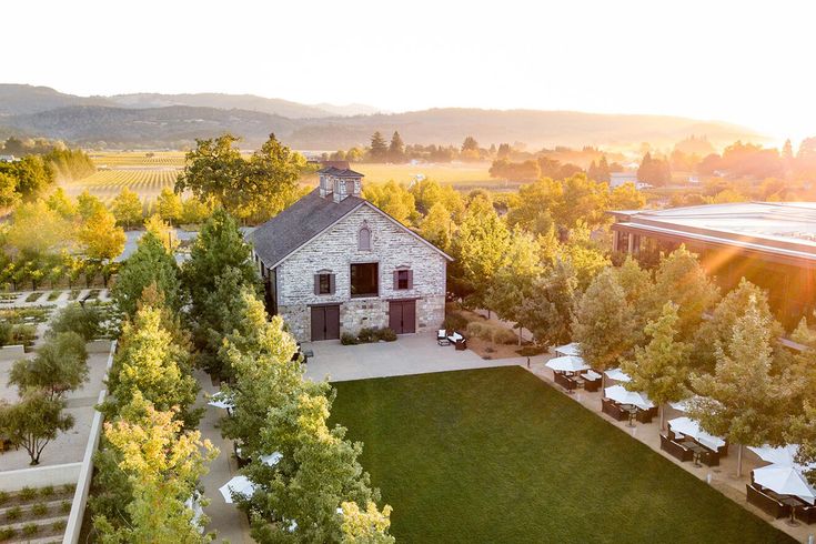 an aerial view of a house surrounded by trees and lawns with the sun setting in the background