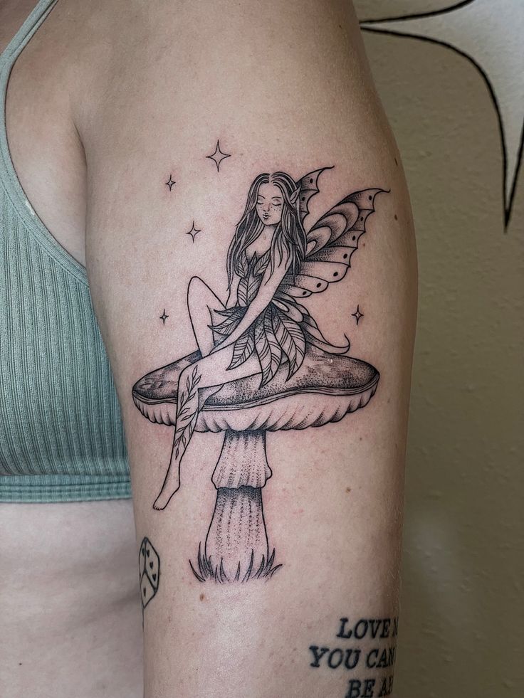 a woman with a tattoo on her arm holding onto a mushroom that has a fairy sitting on it