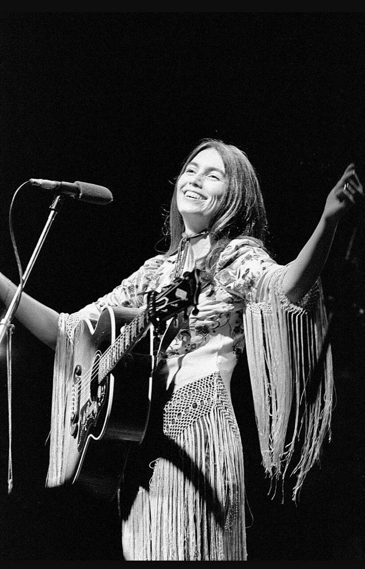 a woman standing in front of a microphone and holding an acoustic guitar with her right hand