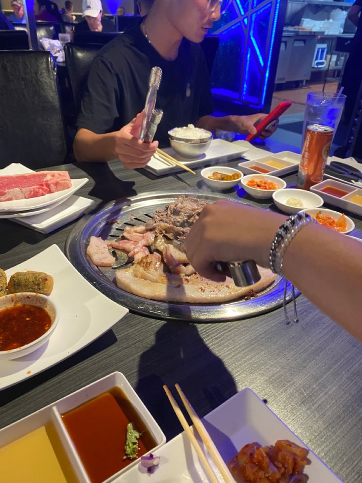 two people sitting at a table with plates of food and chopsticks in front of them