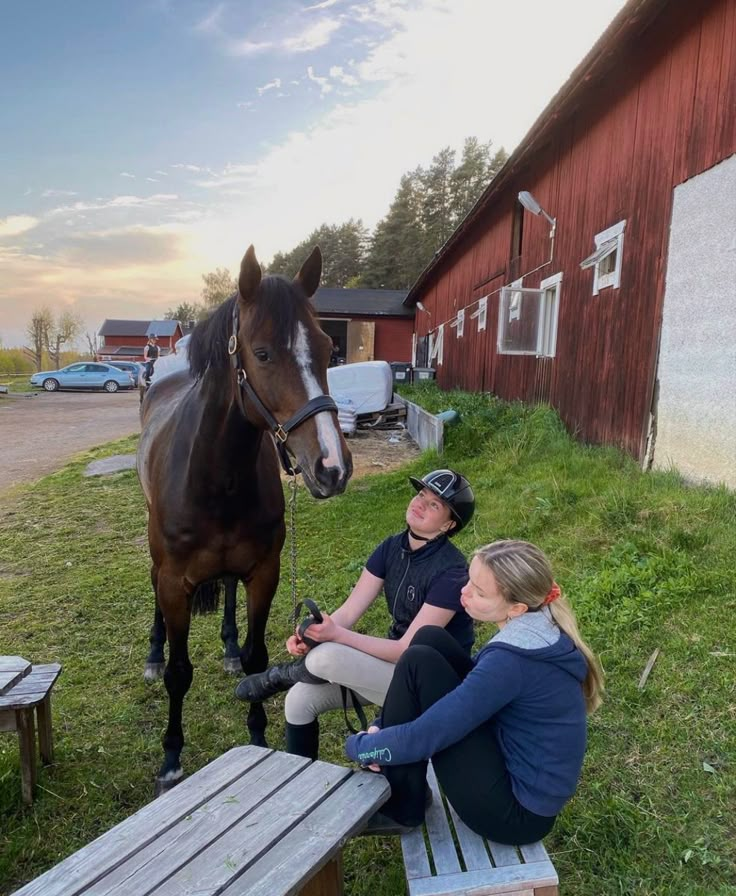 two women sitting on benches next to a horse