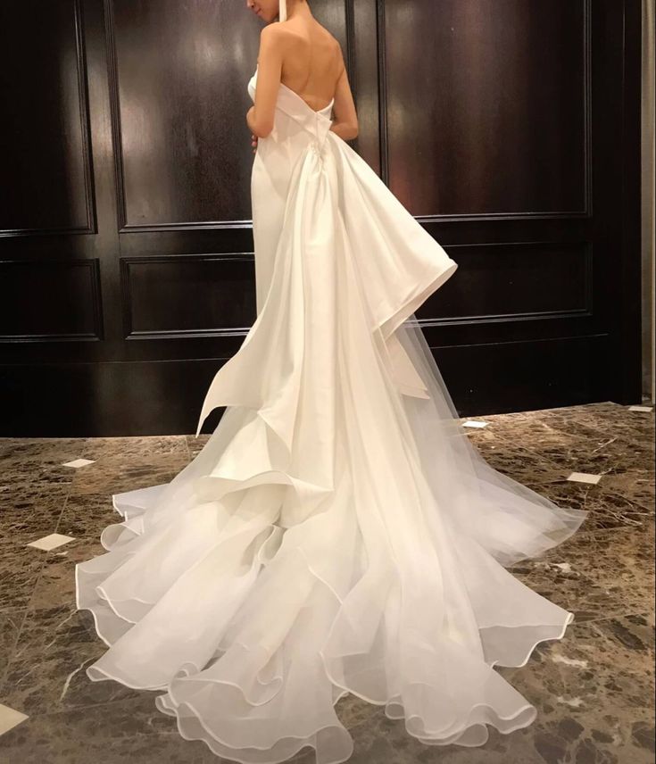 a woman in a white wedding dress standing next to a black door and looking at the floor