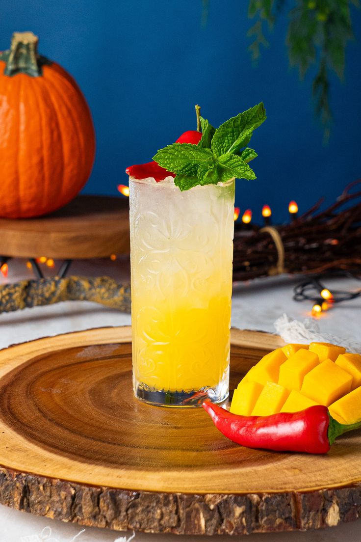 a glass filled with a drink sitting on top of a wooden plate next to a pumpkin