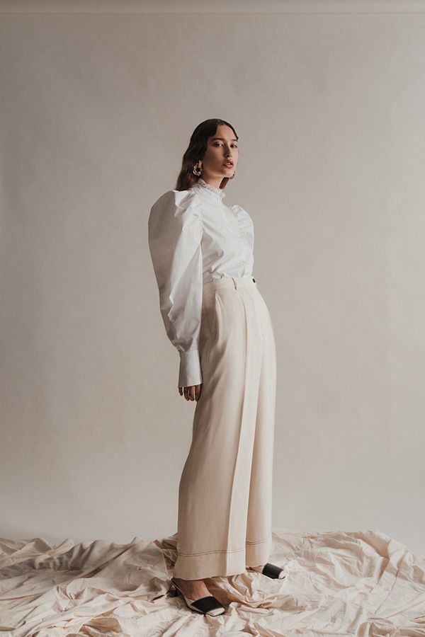 a woman standing on top of a white sheet covered bed wearing high heels and a white blouse