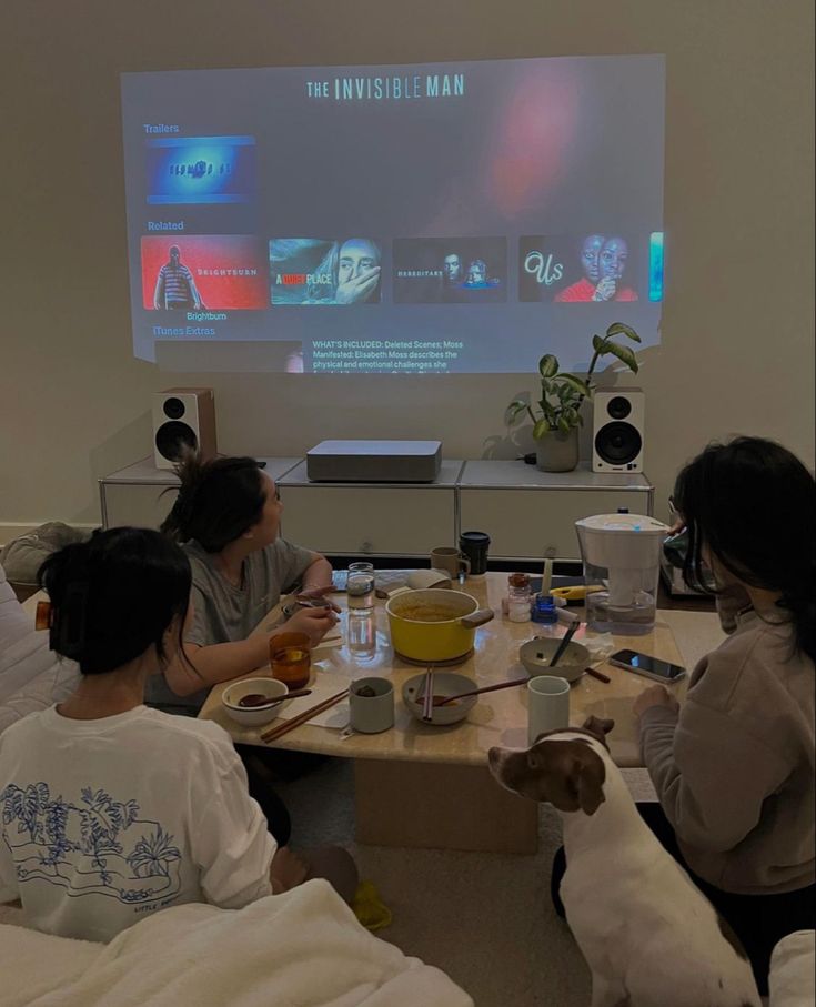 three people sitting at a table with food and drinks in front of a projector screen