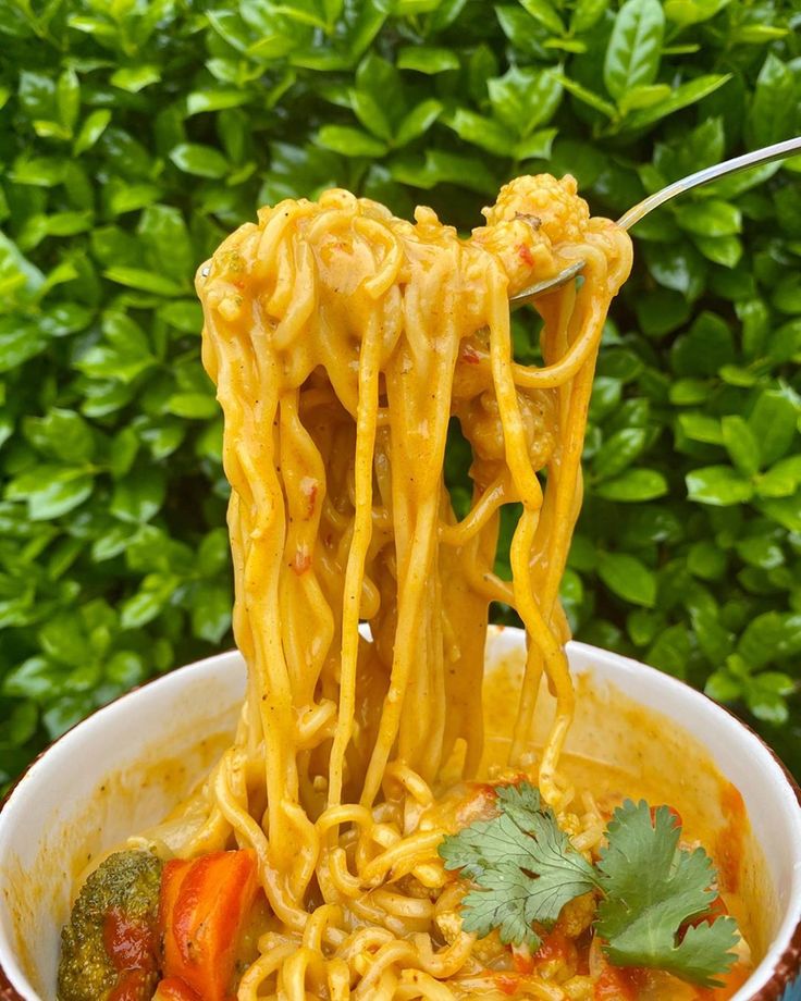 someone is holding up noodles with broccoli and tomatoes to eat it from the bowl