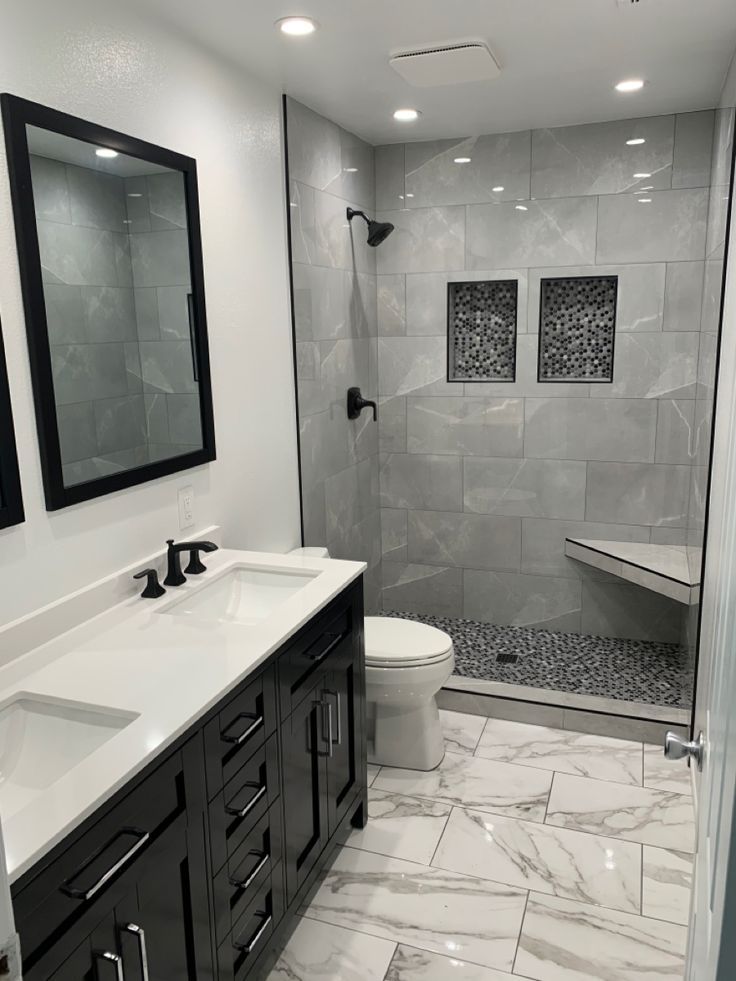 a white and black bathroom with two sinks, mirror, shower stall and marble tile floor